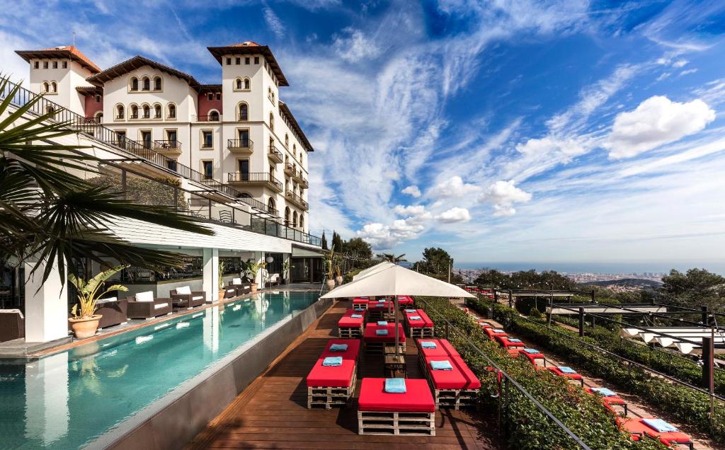a hotel swimming pool with red chairs and umbrellas at Gran Hotel La Florida G.L Monumento in Barcelona