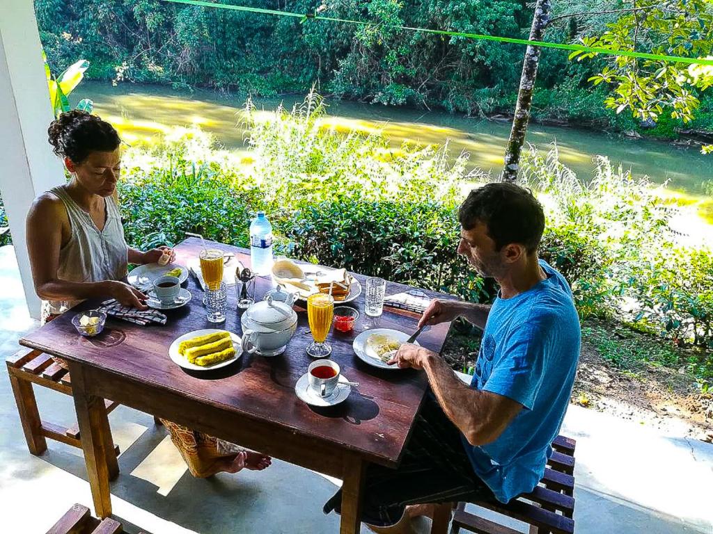 Un uomo e una donna seduti a un tavolo con del cibo di Sinharaja Vini Villa a Deniyaya