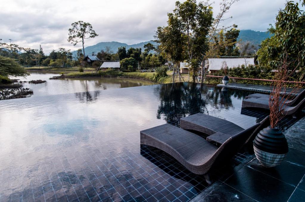 a swimming pool with a bench in front of a lake at Lala Mukha Tented Resort Khao Yai in Mu Si