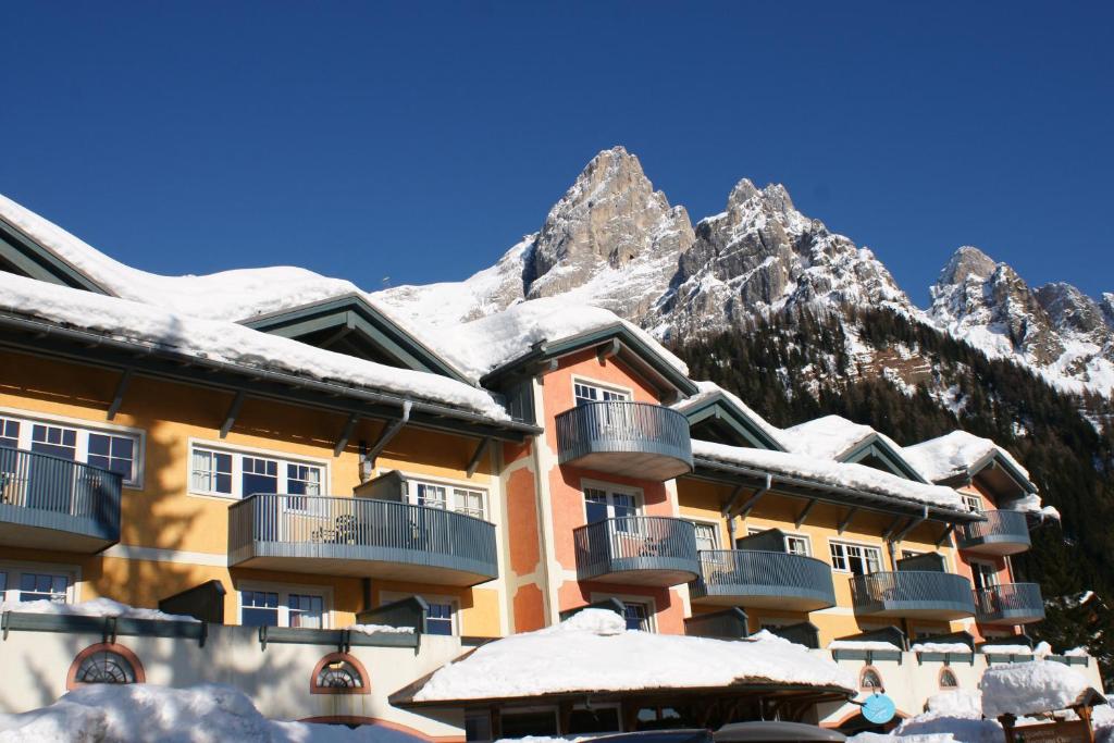 um edifício coberto de neve com montanhas ao fundo em Sporting Clubresidence em San Martino di Castrozza