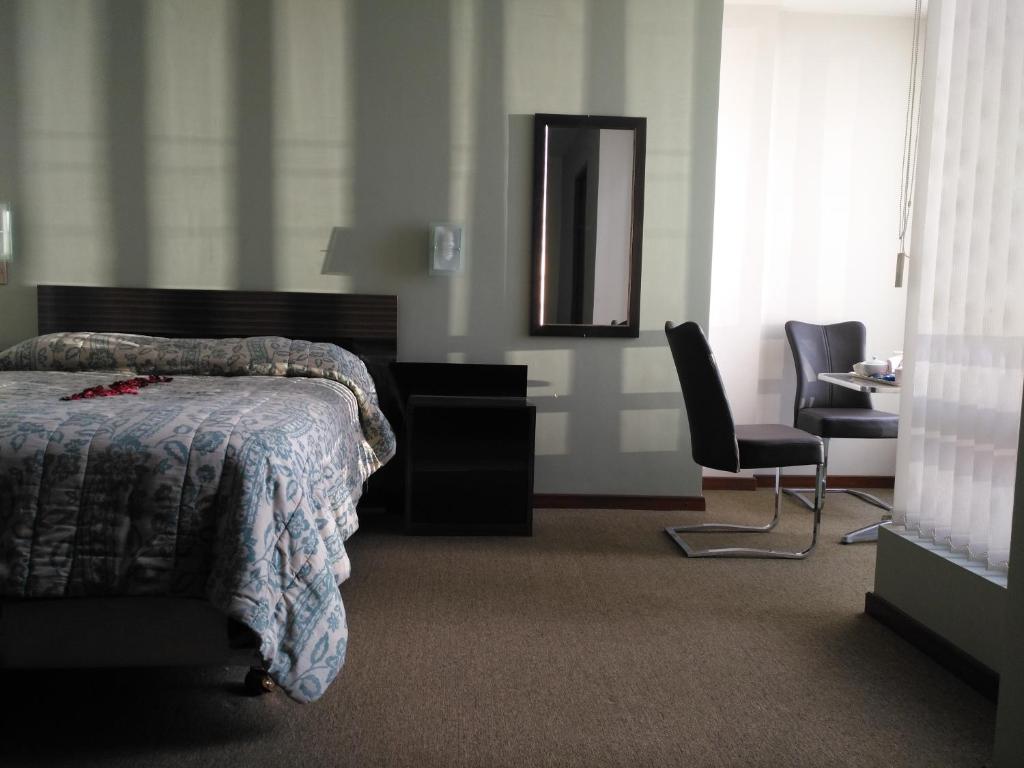 1 dormitorio con cama, espejo y silla en Hostal Costa De Marfil Suites & Apartamentos en Cochabamba