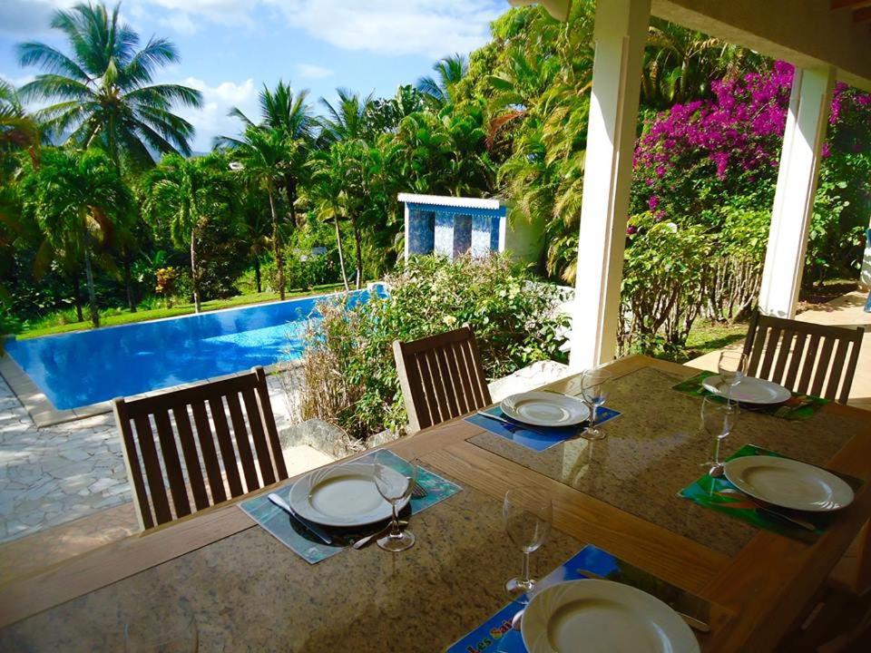 a wooden table with chairs and a table with glasses at Villa LES TILILIS - BELLE VILLA DE 300 M2 SITUEE AU CALME AVEC GRANDE PISCINE ET VUE MONTAGNE in Petit-Bourg