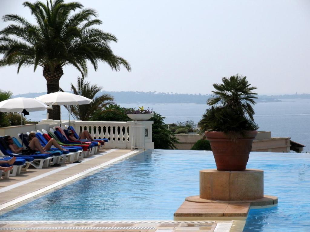 una piscina con sillas, palmeras y agua en La Bastide du Soleil, en Cannes