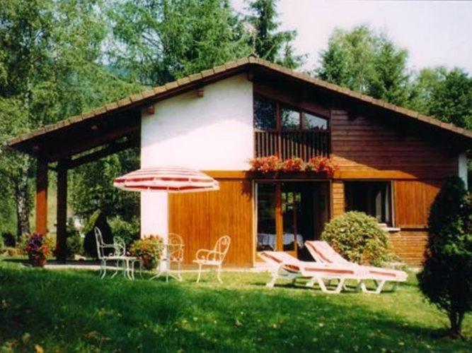 una casa con sedie e ombrellone davanti di Cozy chalet with dishwasher, in the High Vosges a Le Ménil