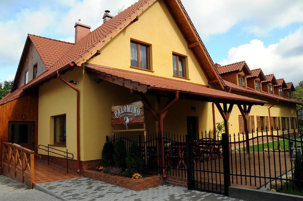 ein gelbes Haus mit einem Zaun davor in der Unterkunft Pensjonat Palomino in Karpacz