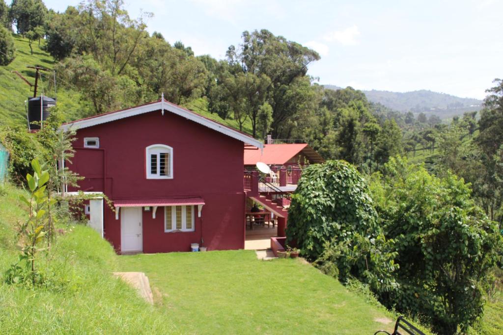 een rood huis op een heuvel met een tuin bij Rustling River Resort in Ooty