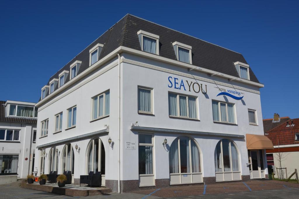 un bâtiment blanc avec un panneau sur son côté dans l'établissement SEA YOU Hotel Noordwijk, à Noordwijk aan Zee