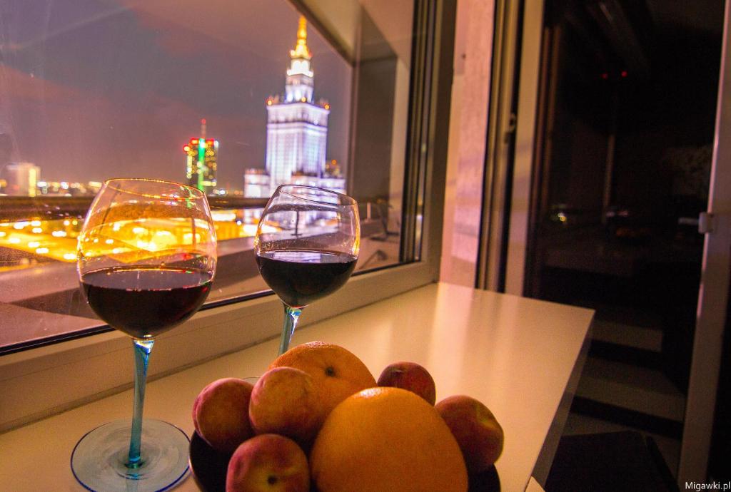 two glasses of wine sitting on a table with fruit at GreatView in Warsaw