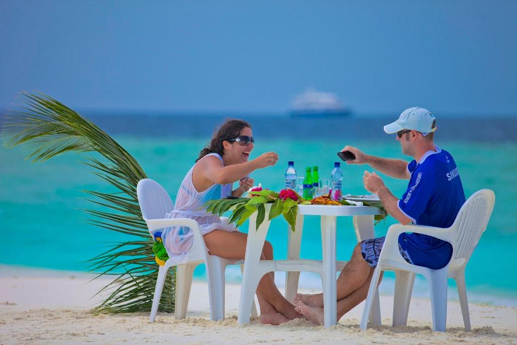 a man and woman sitting at a table on the beach at Kaani Beach Hotel in Maafushi