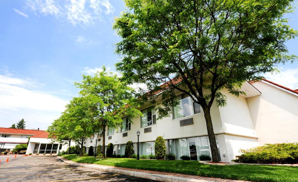 a white building with trees next to a street at Adam's Airport Inn in Ottawa