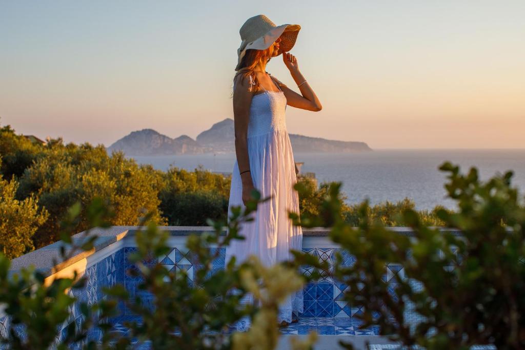 a woman in a white dress and hat looking at the ocean at MelRose Relais in Massa Lubrense