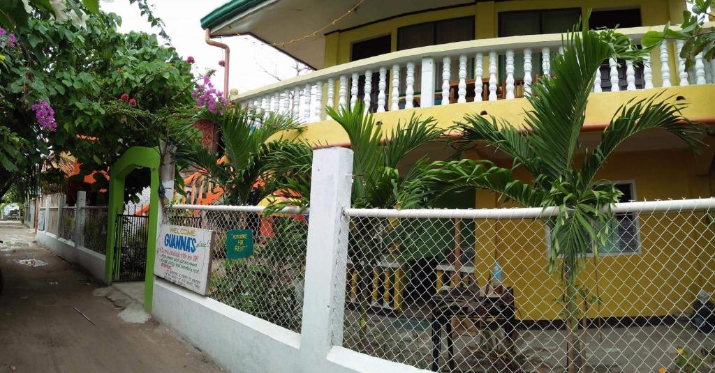 a fence in front of a yellow house with plants at Guanna's Place Room and Resto Bar in Malapascua Island