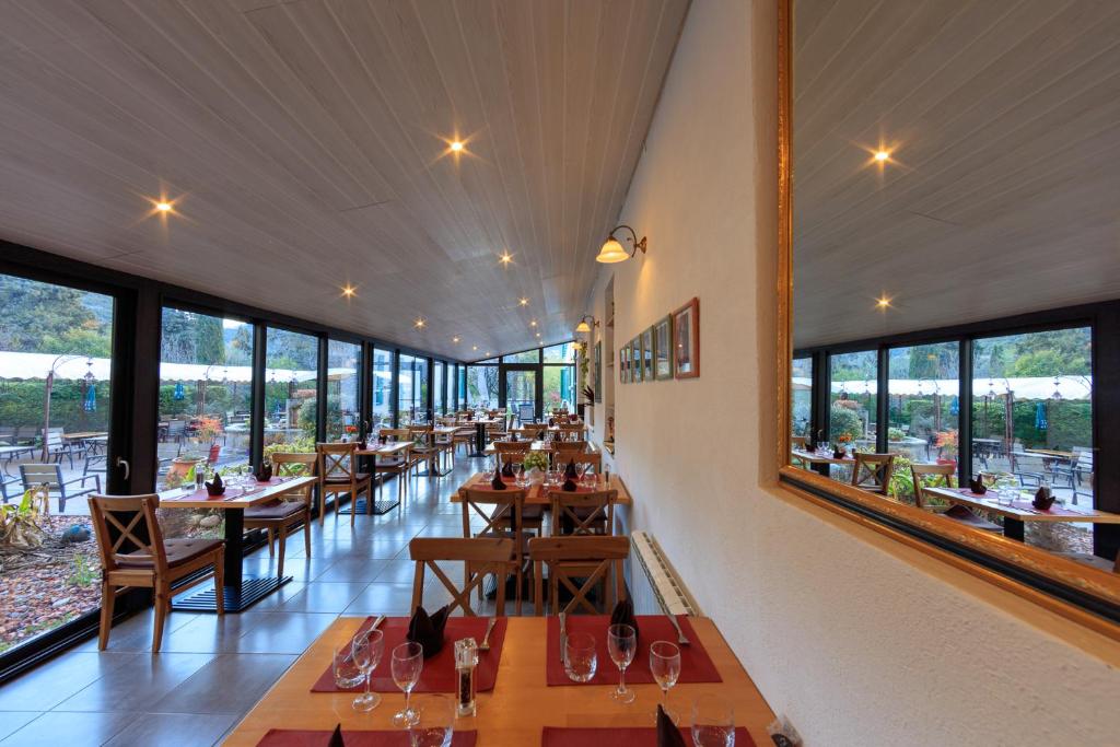 a restaurant with tables and chairs and large windows at Hotel Carmel in Les Vans