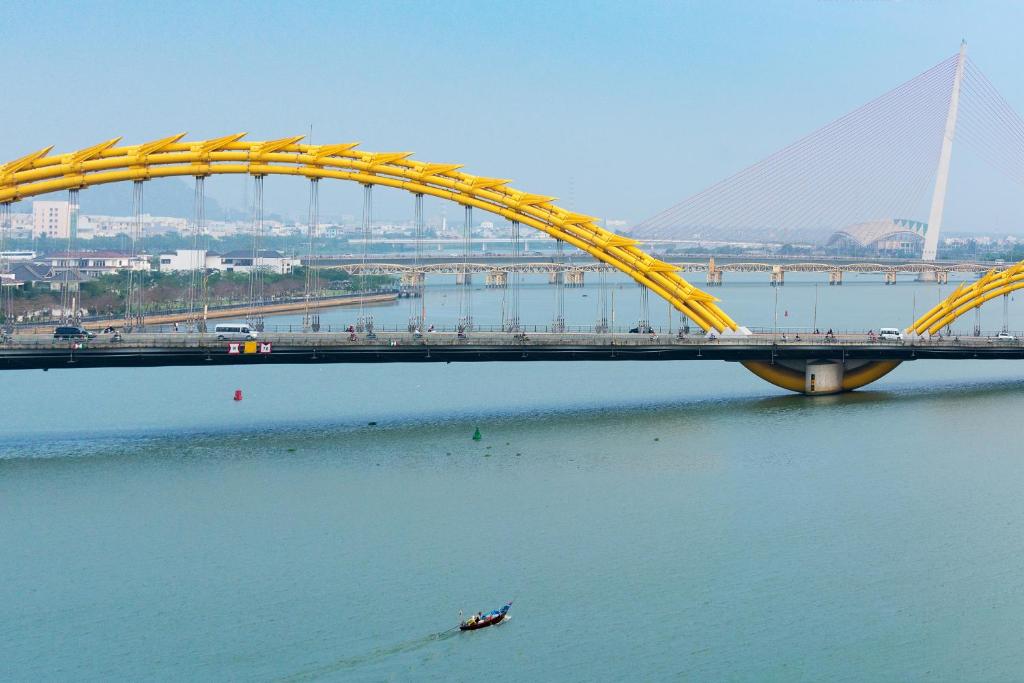 a bridge over the water with a boat under it at Happy Day Riverside Hotel & Spa Danang by Haviland in Danang
