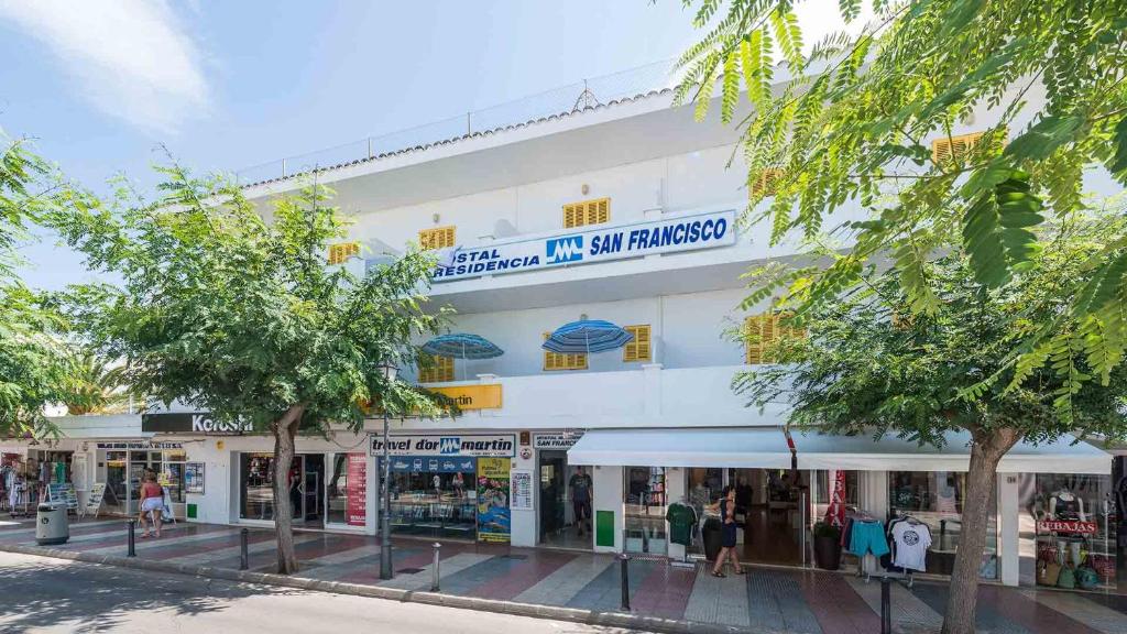 a building on a street with trees in front of it at Hostal San Francisco in Cala d´Or