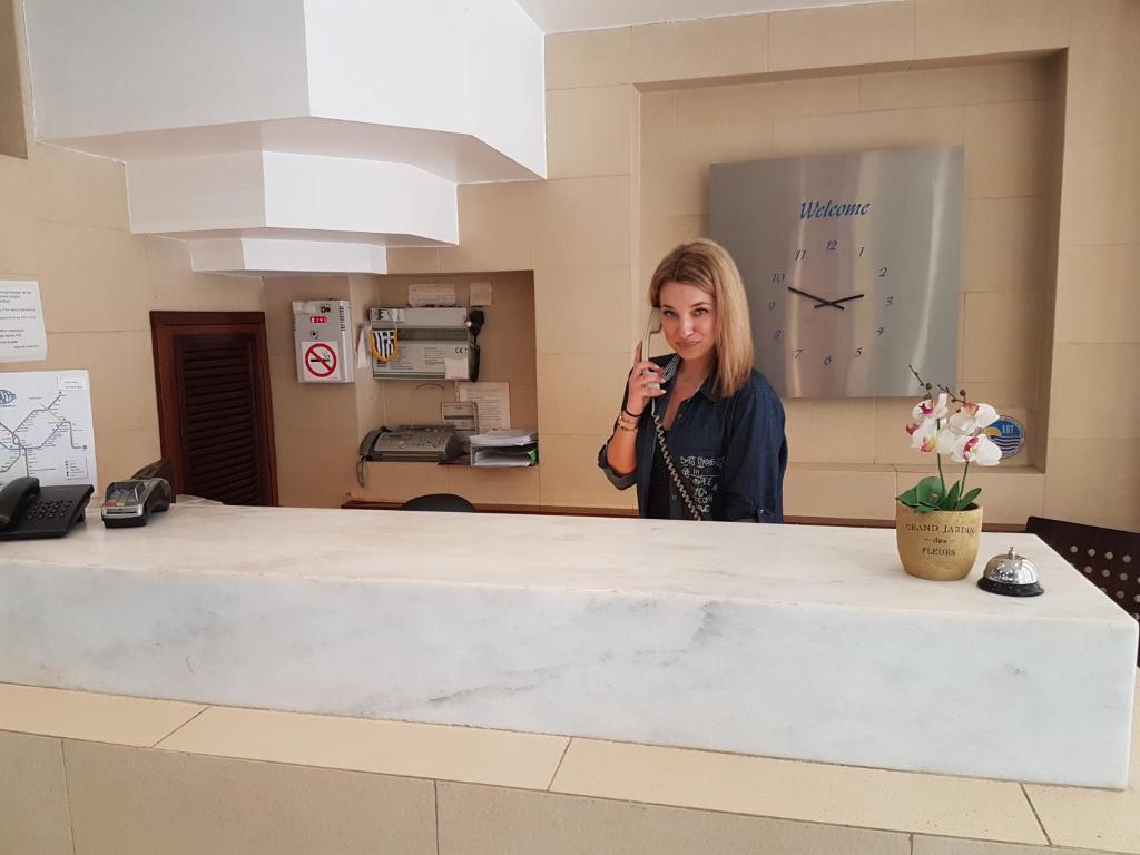 a woman standing behind a counter talking on a cell phone at Hotel Ideal in Piraeus