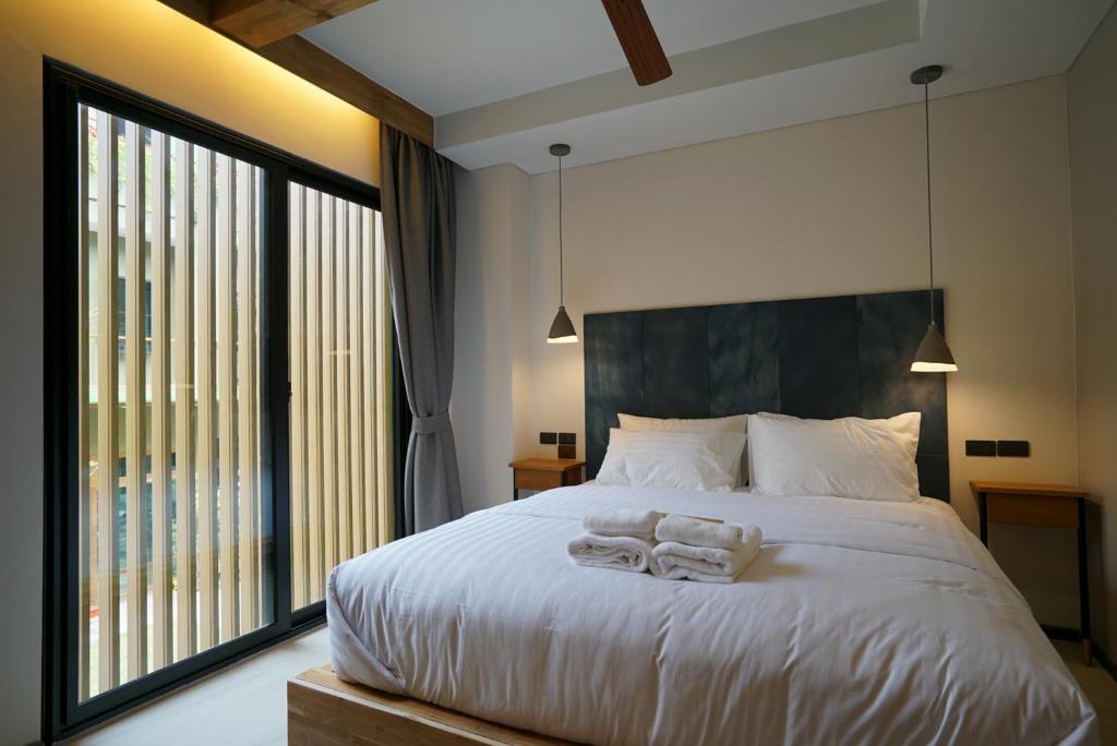 A bright double bedroom with a large bed, ceiling fan, pendant lights, and a tall glazed opening.