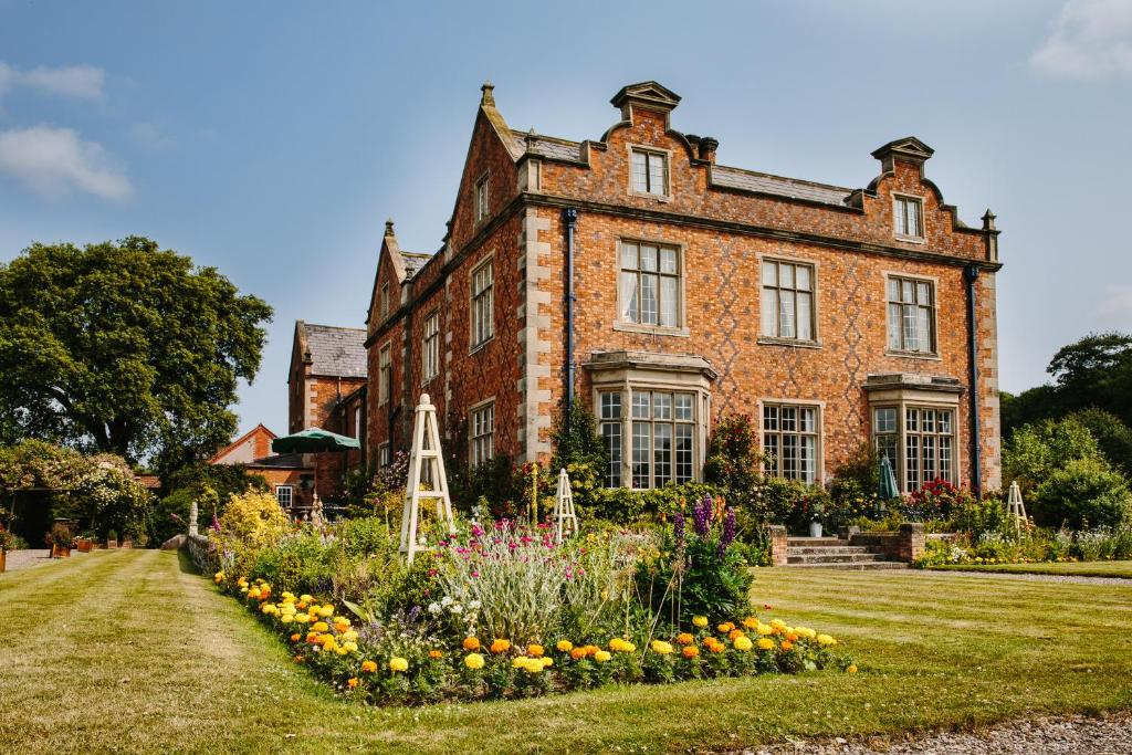 uma antiga casa de tijolos com um jardim em frente em Willington Hall Hotel em Tarporley