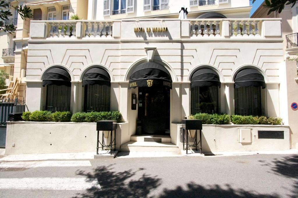 un edificio blanco con una puerta negra y algunas plantas en Hotel De Monaco, en Cap d'Ail
