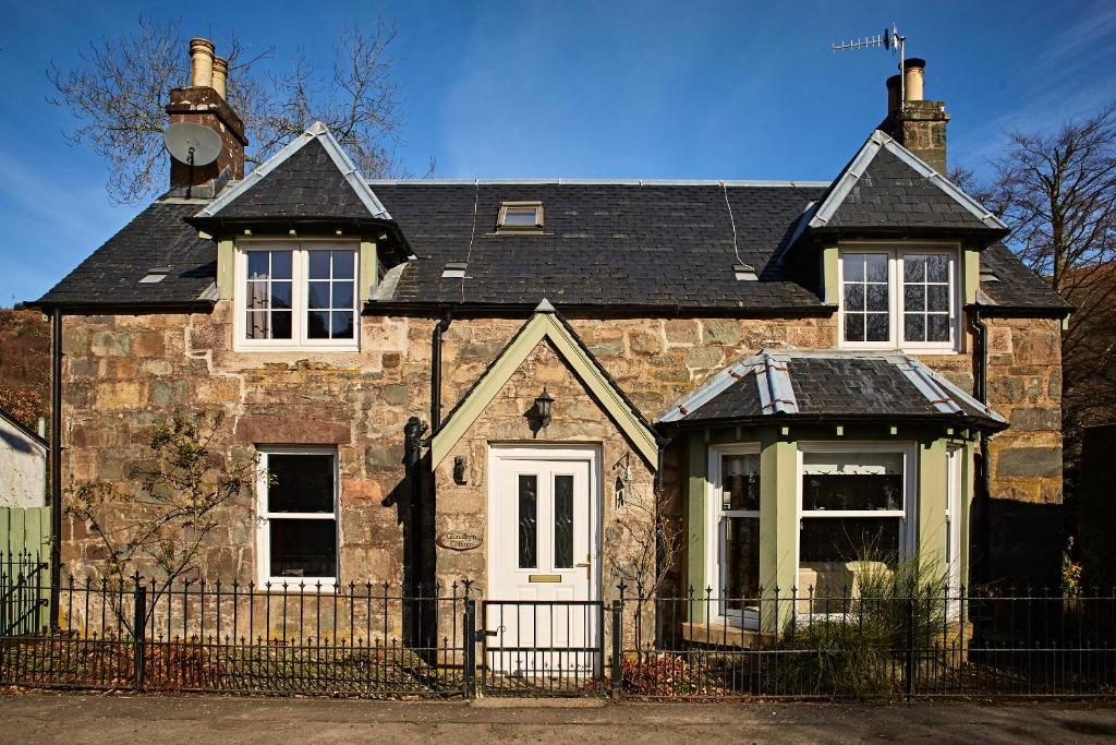 uma antiga casa de pedra com um telhado preto em Glenalbyn Cottage em Saint Fillans