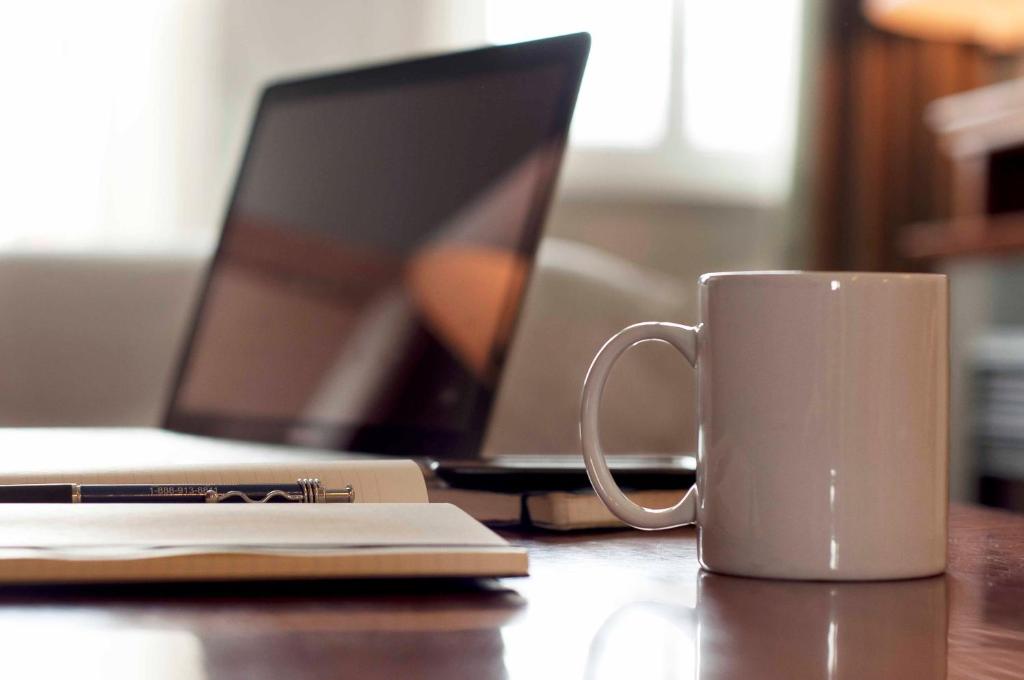 a white coffee cup sitting on a table with a laptop at Summit Lodge Boutique Hotel by Paradox in Whistler