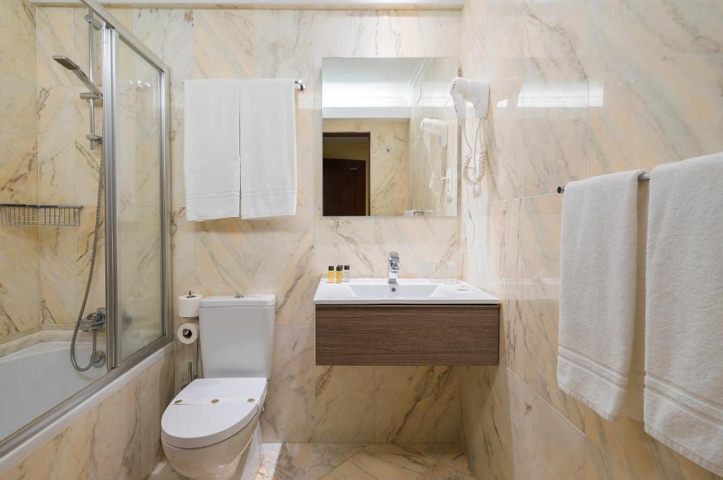 a white toilet sitting next to a bath tub in a bathroom at Hotel Internacional Porto in Porto