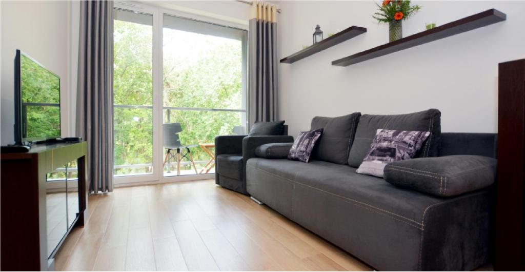 a living room with a black couch and a large window at DWIE SOSNY Apartament 52 in Ustronie Morskie