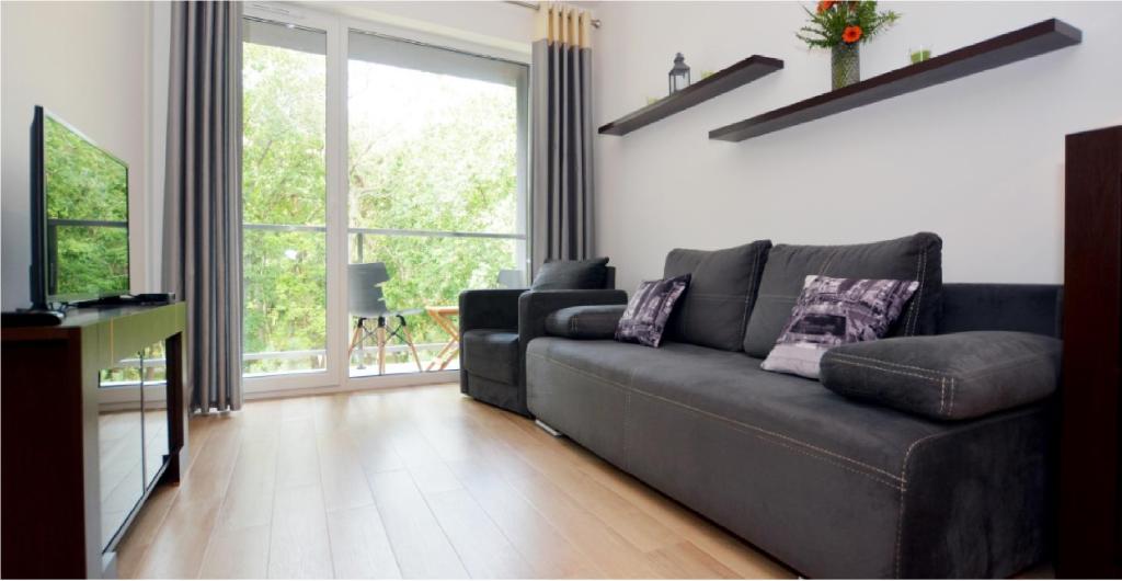 sala de estar con sofá negro y ventana grande en DWIE SOSNY Apartament 52, en Ustronie Morskie