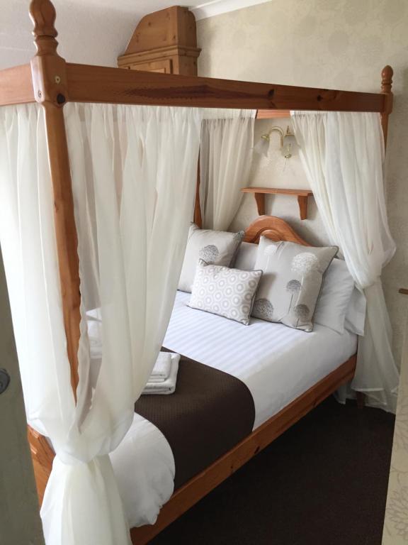 Woodthorpe Hotel في سكيجنيس: غرفة نوم مع سرير مظلة مع ستائر بيضاء
