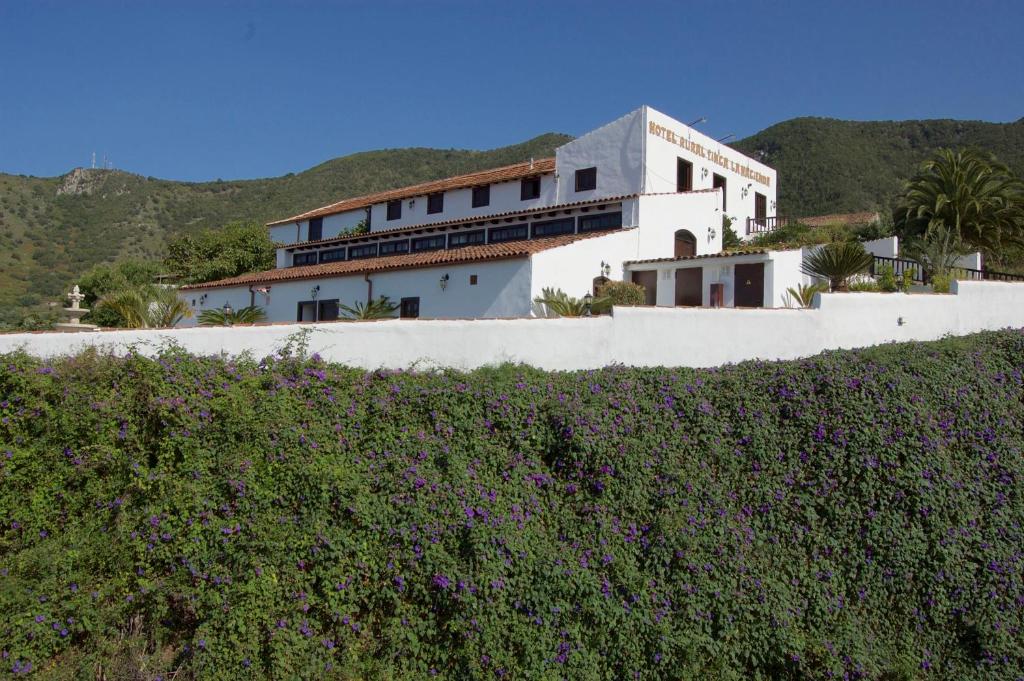 une maison blanche avec une haie en face d'un bâtiment dans l'établissement Hotel Rural Finca La Hacienda, à Los Silos