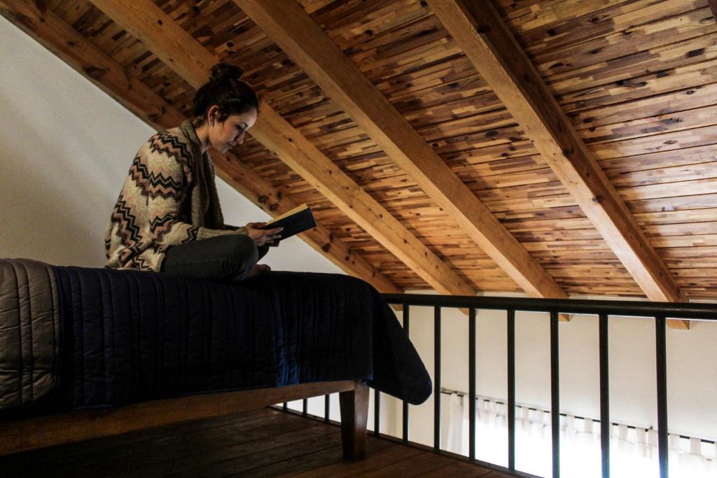 uma mulher sentada numa cama a ler um livro em Hotel María del Tío Molcas em Creel