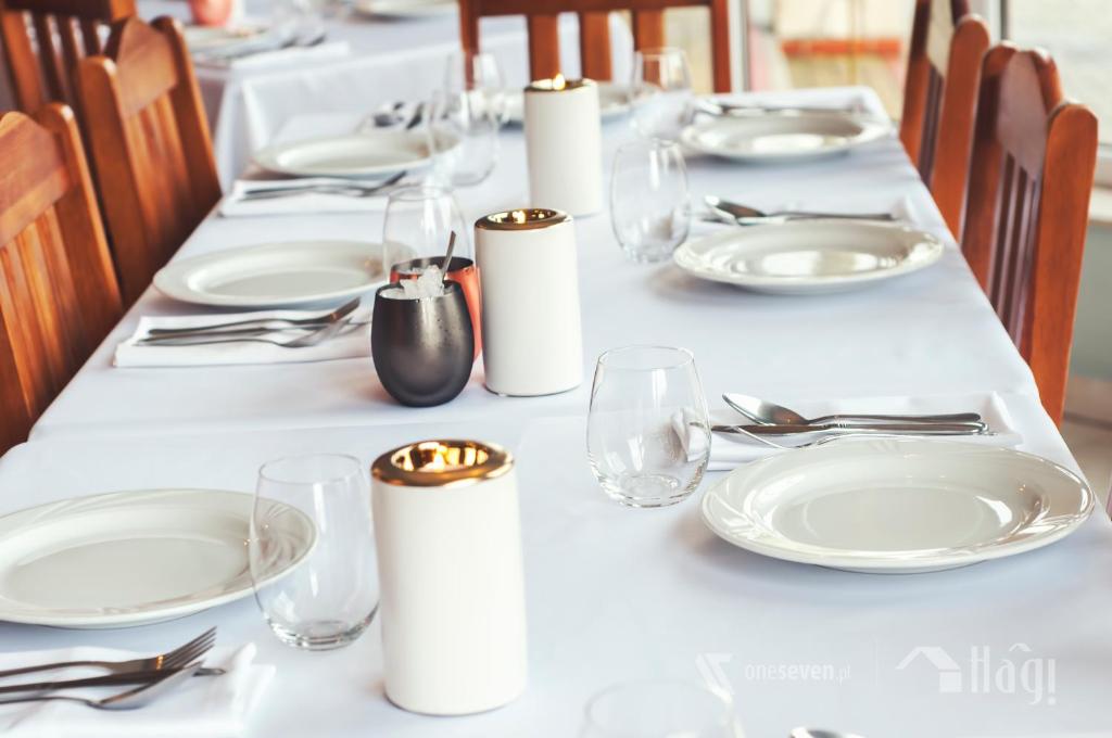 une grande table avec des assiettes et des verres blancs et de la argenterie dans l'établissement Pensjonat Hagi, à Horyniec