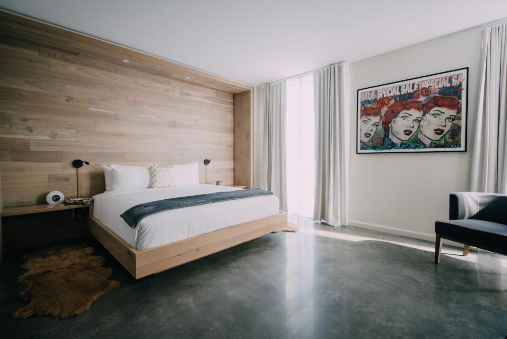 A photo of one room at the Preston House & Hotel, featuring an all-natural wood accent wall behind the king sized bed which sits in a large open room with dark (concrete?) floors.