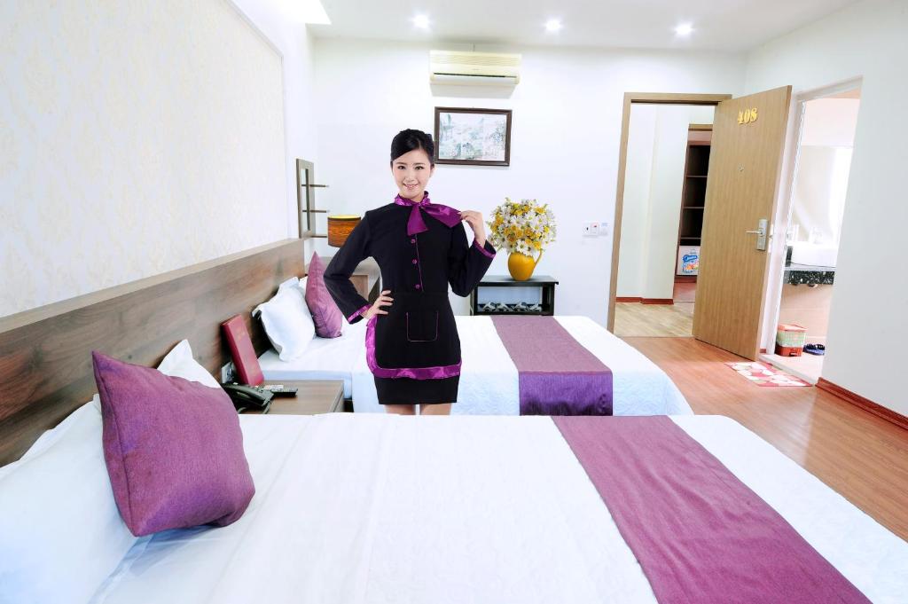 ニンビンにあるVan Giang Hotelの女性がホテルの部屋のベッド2台の横に立っている