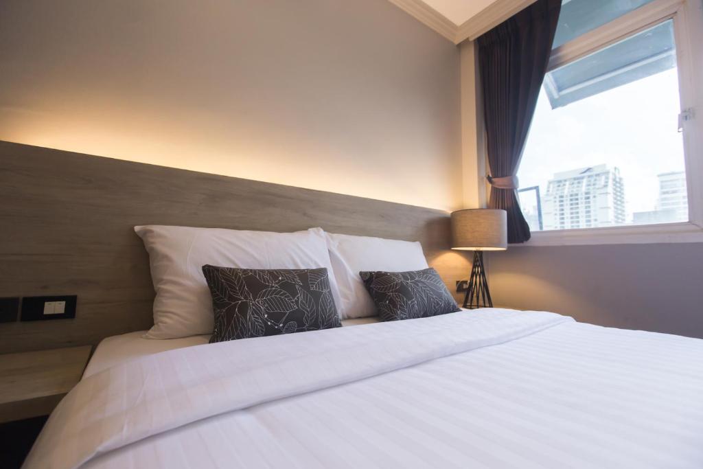 a bedroom with a white bed with pillows and a window at Maxim's Inn in Bangkok