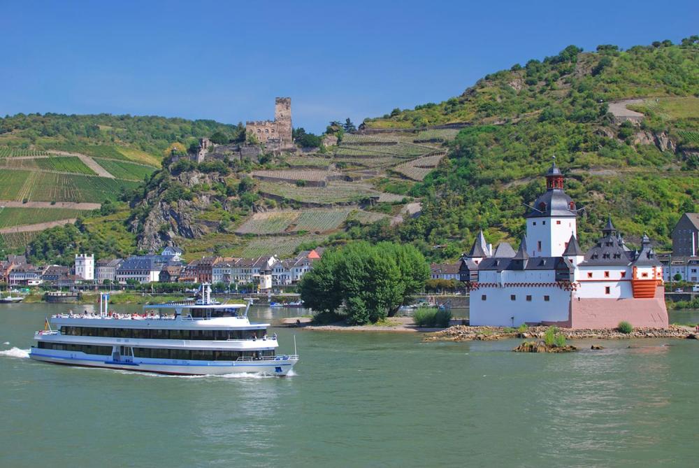 a cruise ship in the water next to a castle at Rheinpromenade in Kamp-Bornhofen