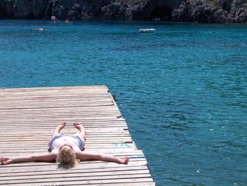 Eine Frau, die auf einem Steg im Wasser liegt. in der Unterkunft Paraskevi Apartments in Paleokastritsa