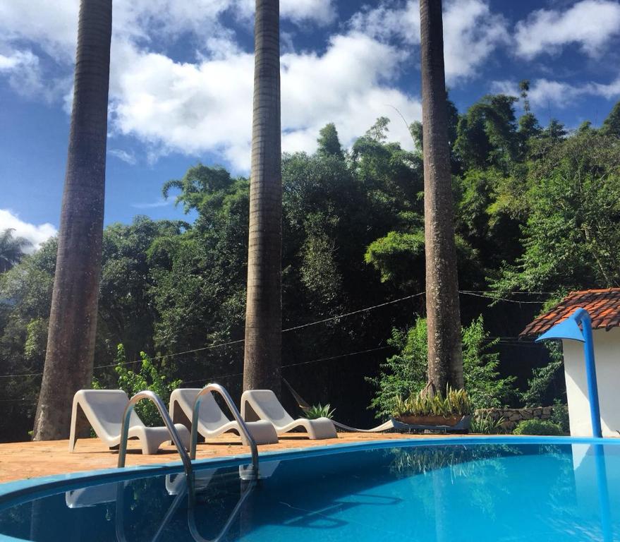 a swimming pool with two chairs and palm trees at Pousada Cantinho do Mundo in Brumadinho