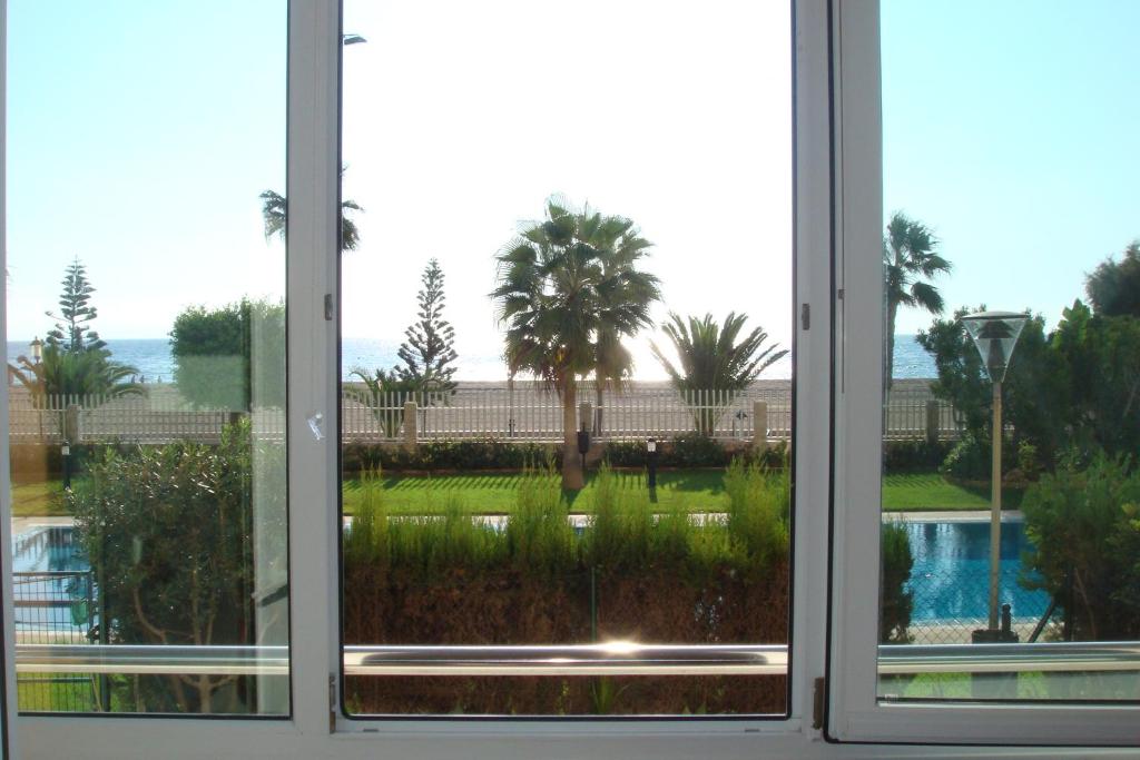 a window with a view of a pool and palm trees at Primera línea playa in Roquetas de Mar