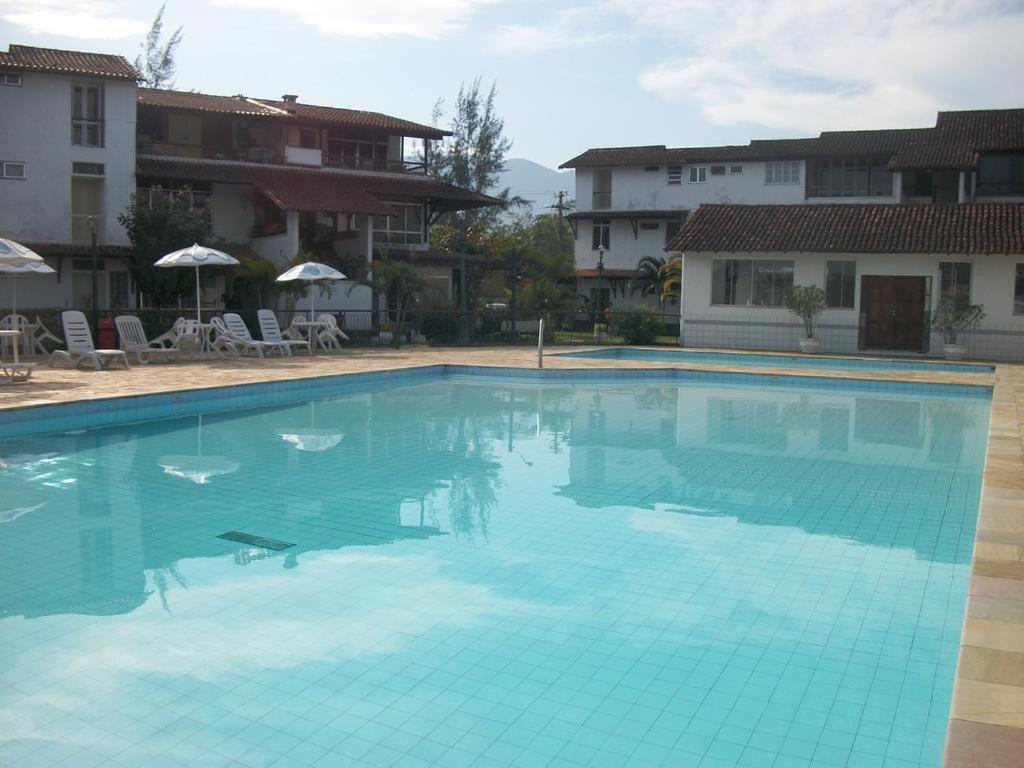 a large blue swimming pool with chairs and umbrellas at Apartamento Porto Bracuy Apartment in Angra dos Reis