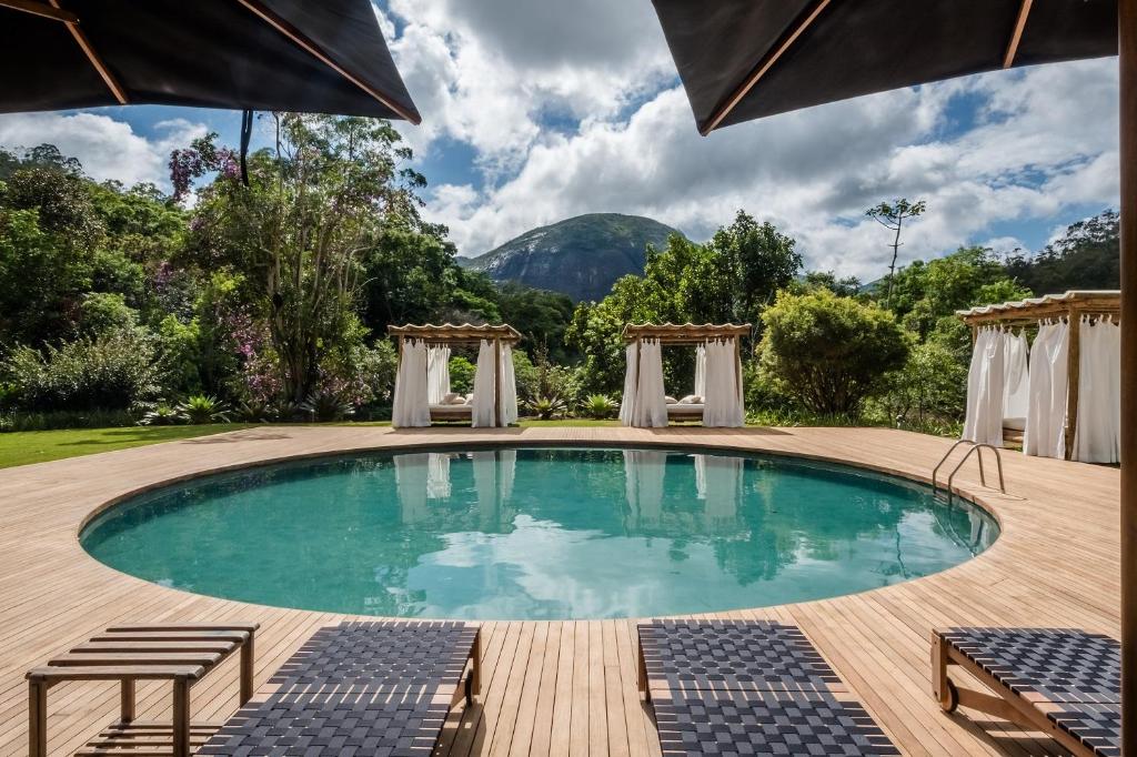 uma piscina com um deque e cadeiras e uma montanha em Pousada Tankamana em Itaipava