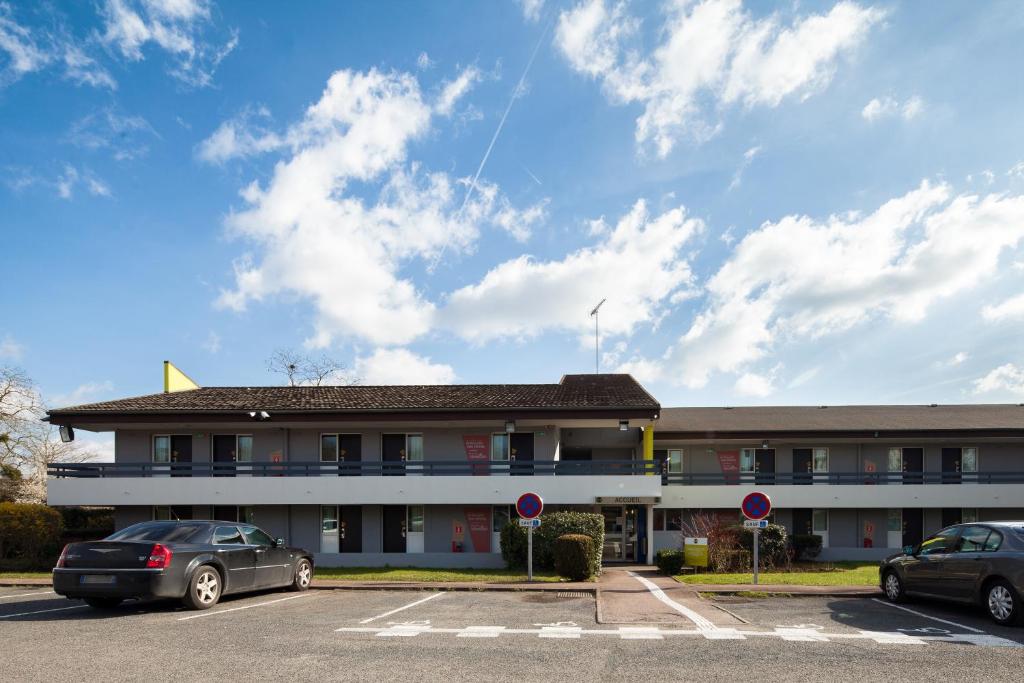 een gebouw met twee auto's geparkeerd op een parkeerplaats bij B&B HOTEL Corbeil-Essonnes in Corbeil-Essonnes