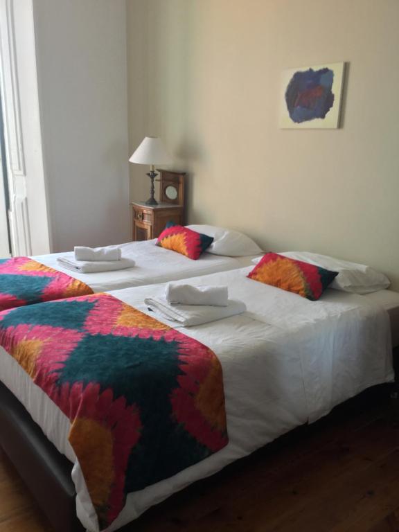 Duas camas num quarto com lençóis brancos e almofadas coloridas em Varandas do Marquês em Lisboa