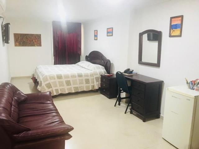 a bedroom with a bed and a desk and a couch at Hotel Tarento Suite in Barranquilla