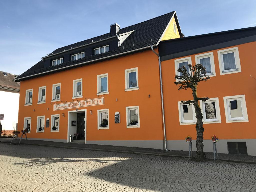 un bâtiment orange avec un arbre devant lui dans l'établissement Gasthof zum Waldstein, à Zell im Fichtelgebirge
