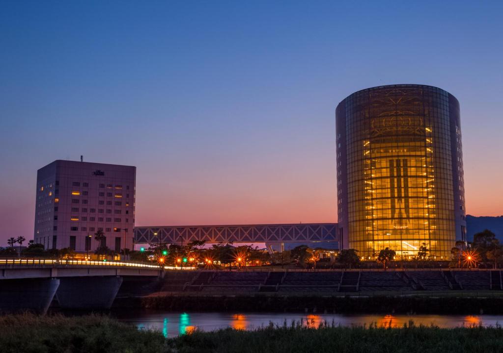 雾岛市京瓷酒店的一座高大的建筑,靠近一条有桥的河流