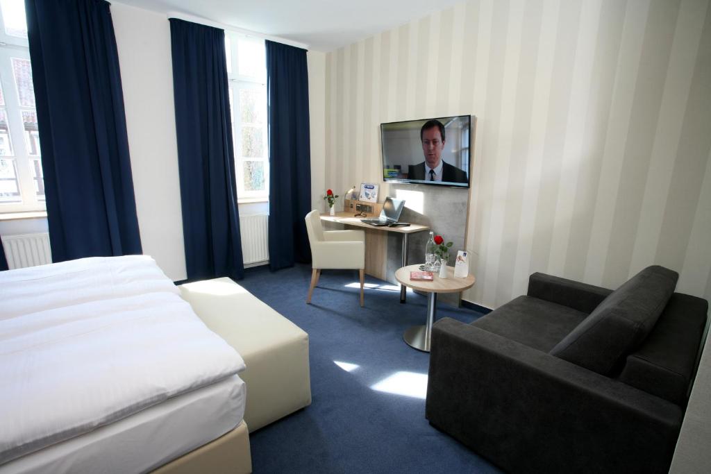 een hotelkamer met een bed, een bank en een tv bij Nigel Restaurant & Hotel im Wendland in Bergen an der Dumme