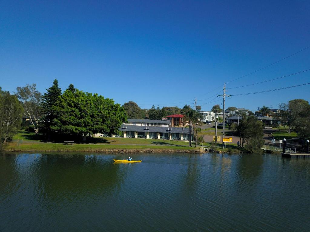 a yellow boat in the water near a house at Hibiscus Lakeside Motel in Budgewoi