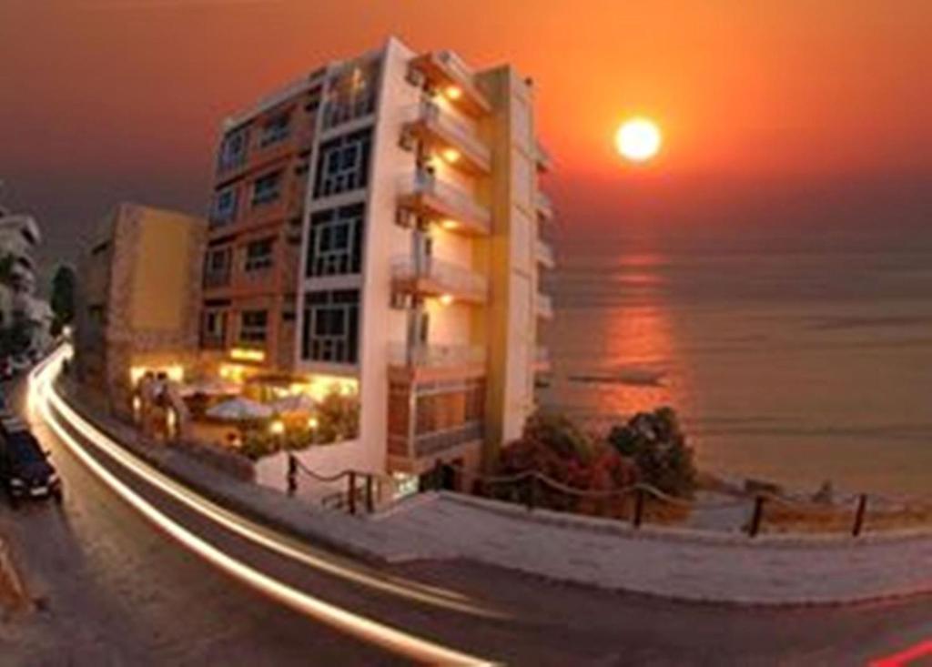 un grand bâtiment avec le coucher du soleil en arrière-plan dans l'établissement Ahiram Hotel Byblos, à Byblos