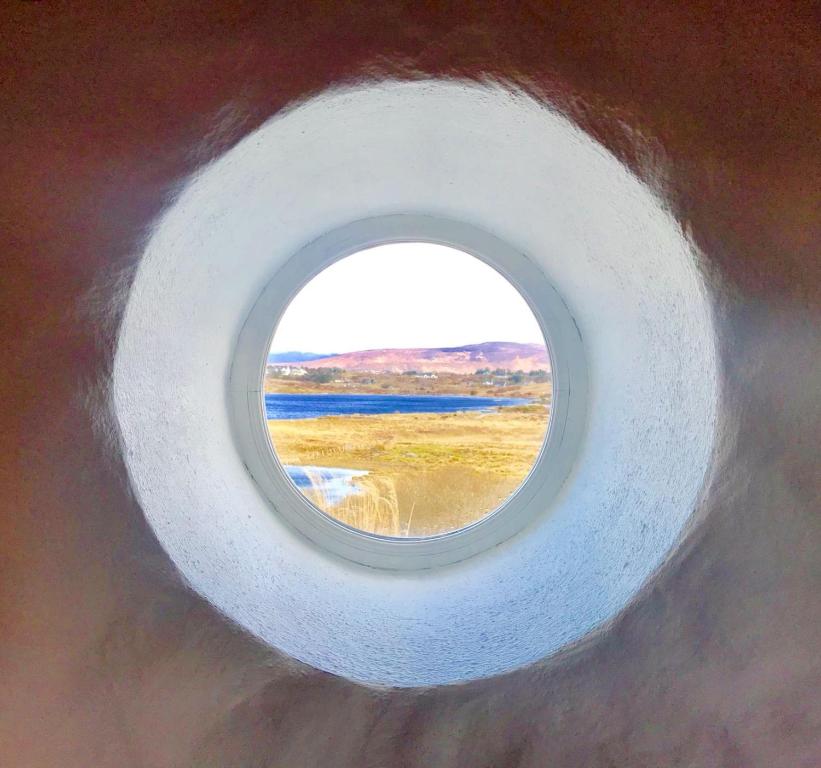 a round window in a wall with a view of the ocean at Ned's Cottage in Kincasslagh